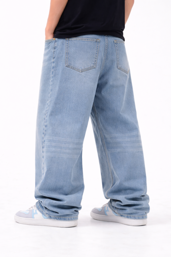 Back view of men’s light blue oversized fit denim jeans with relaxed streetwear style and casual white-blue sneakers.