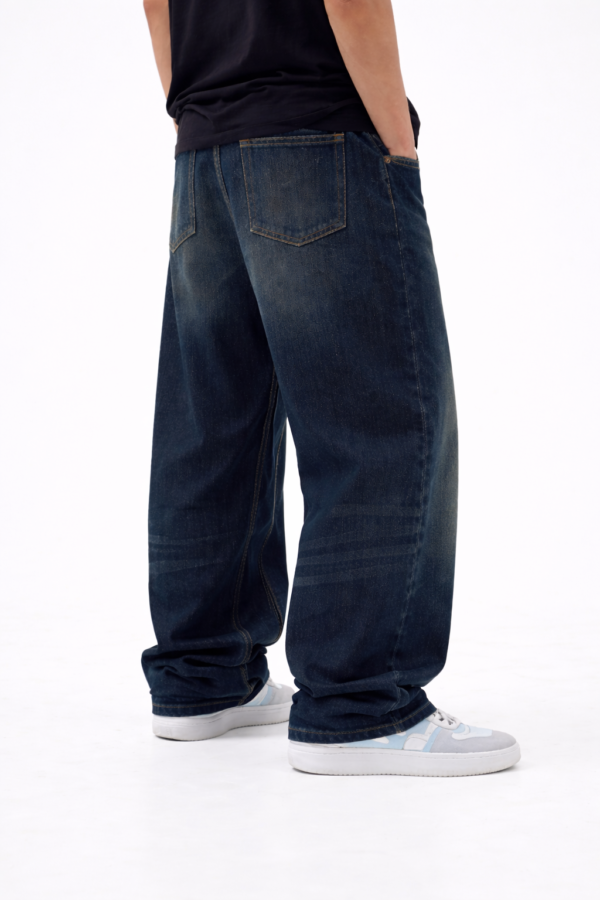 Back view of men’s dark blue oversized fit denim jeans with relaxed streetwear style and casual sneakers.